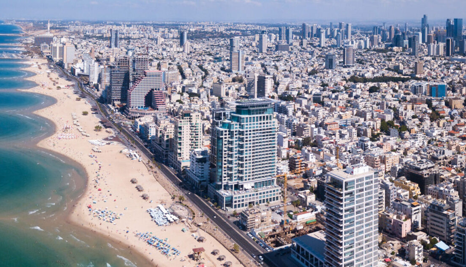 Aerial view of a coastal city with a curved sandy beach, high-rise buildings, and dense urban area.