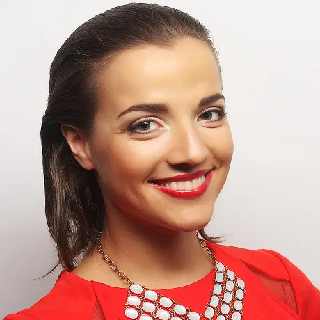 Smiling woman with slicked-back hair wearing a red top and a white statement necklace.